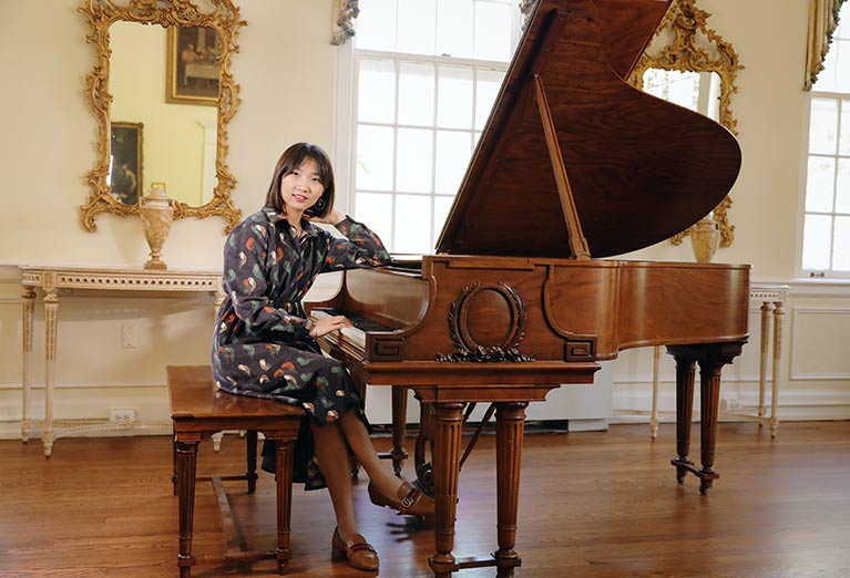 Valentina Huang sits at the piano in the Burden Parlor on campus.