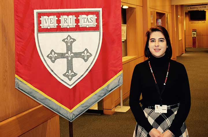 Maria stands in front of Harvard flag.