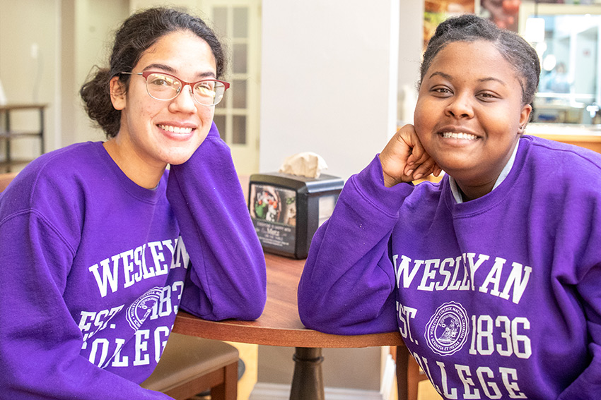 two students sitting at table with purple sweatshirts on