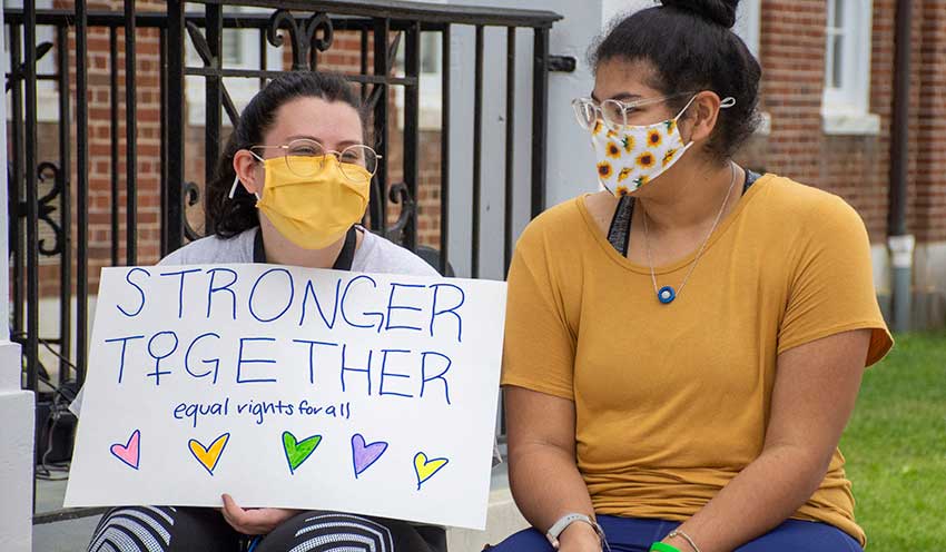 Two students hold up a sign that says Stronger Together