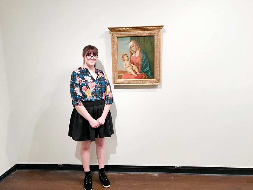 Art History major stands in front of painting in Wesleyan collection.