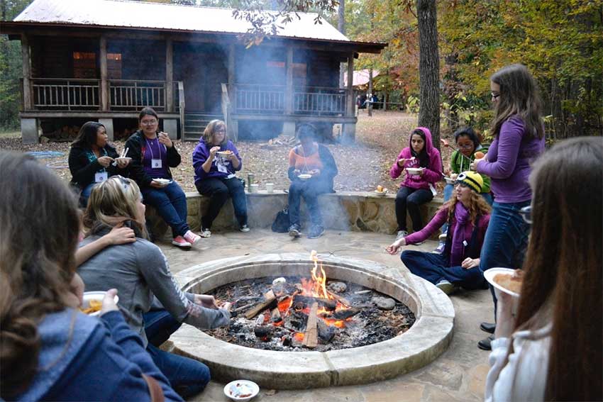 People sit around the firepit with the cabin int he background.