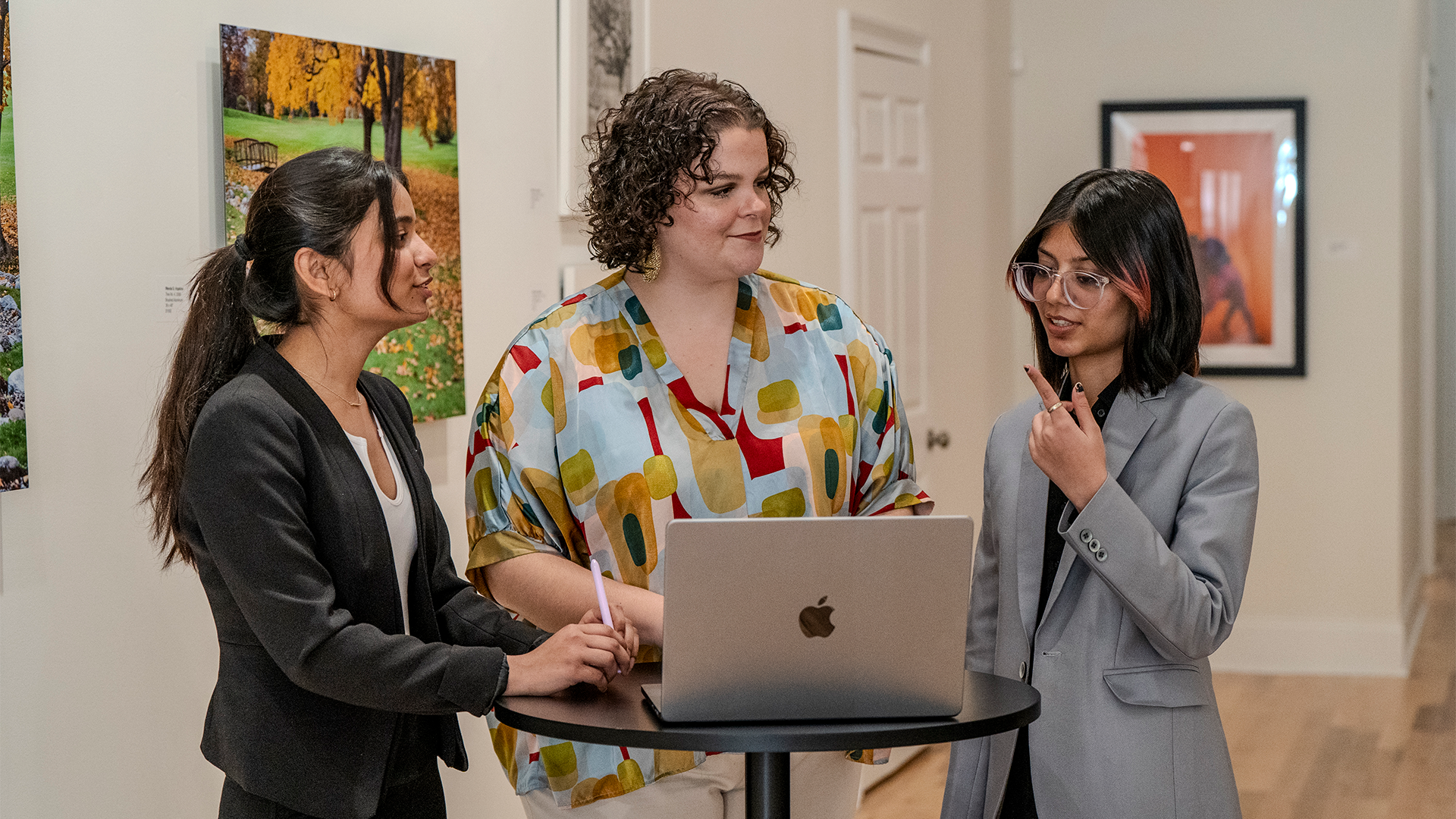3 students in front of a laptop, conversing about a project
